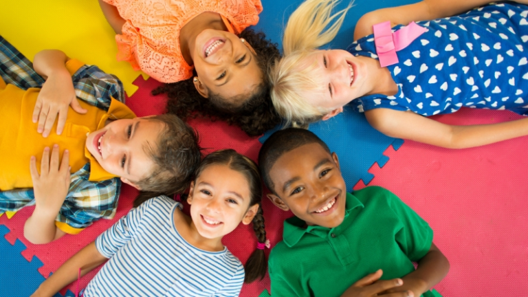 Smiling children lying together on colorful play mats at MidWay ABA in Carmel, Indiana, where compassionate therapists provide personalized autism therapy and brain-based learning support.