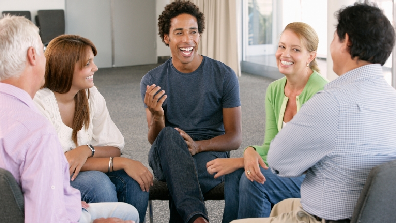 A group of parents sitting together in a supportive circle, smiling and sharing experiences during a MindWay ABA parent support group in Carmel, Indiana.