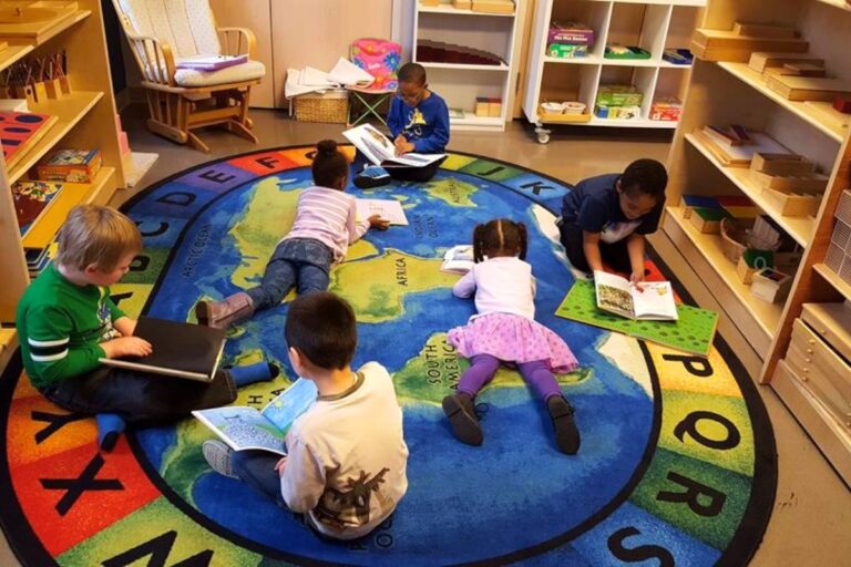 A group of young children read books together on a bright, world map rug in a classroom at MindWay ABA’s Learning Center, surrounded by shelves of educational materials and learning tools.