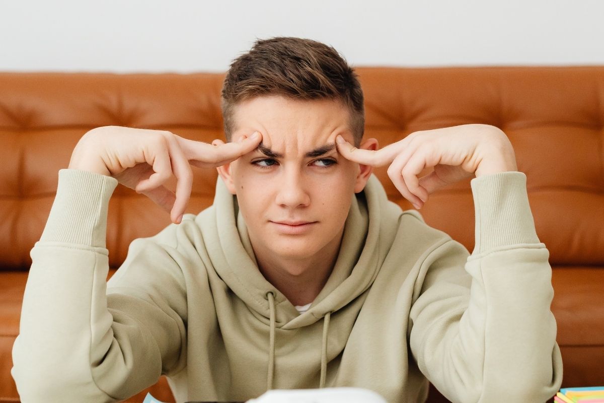 A teenage boy in a light hoodie concentrating with his fingers on his temples, symbolizing focus and attention during an ADHD brain mapping session at MindWay in Carmel, Indiana.